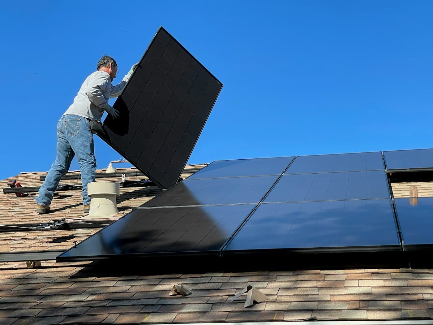 An installer lifts a solar panel into place on a shingled roof